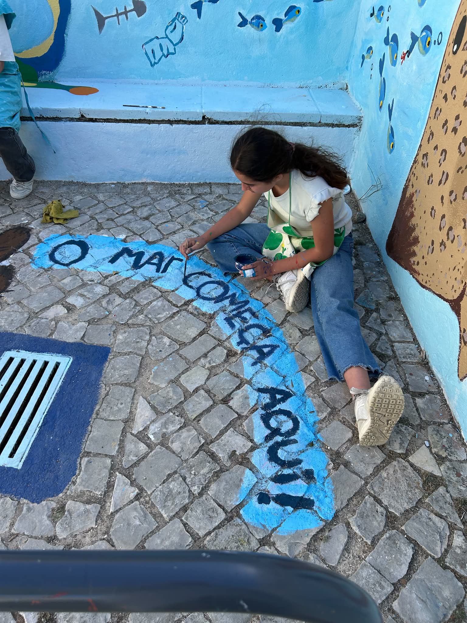 Pintura da frase «O Mar Começa Aqui» em tons de azul, integrando-se harmoniosamente na composição e remetendo para a ligação entre os cursos de água e o oceano.